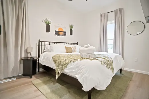 King bedroom with a black spindle bed frame, neutral walls, a round mirror, and a curtained window.