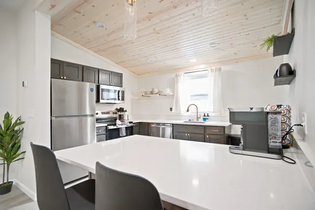 Kitchen with dark cabinets, white countertops, stainless refrigerator, and a wood-plank ceiling.