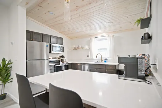 Kitchen with dark cabinets, white countertops, stainless refrigerator, and a wood-plank ceiling.