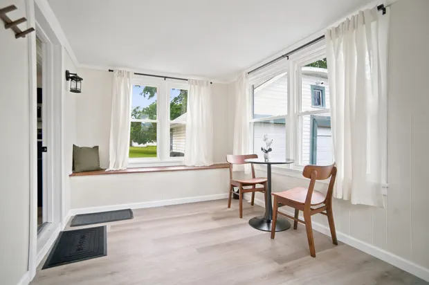 Sunroom with white walls, a window bench, and a small bistro table with two wooden chairs.