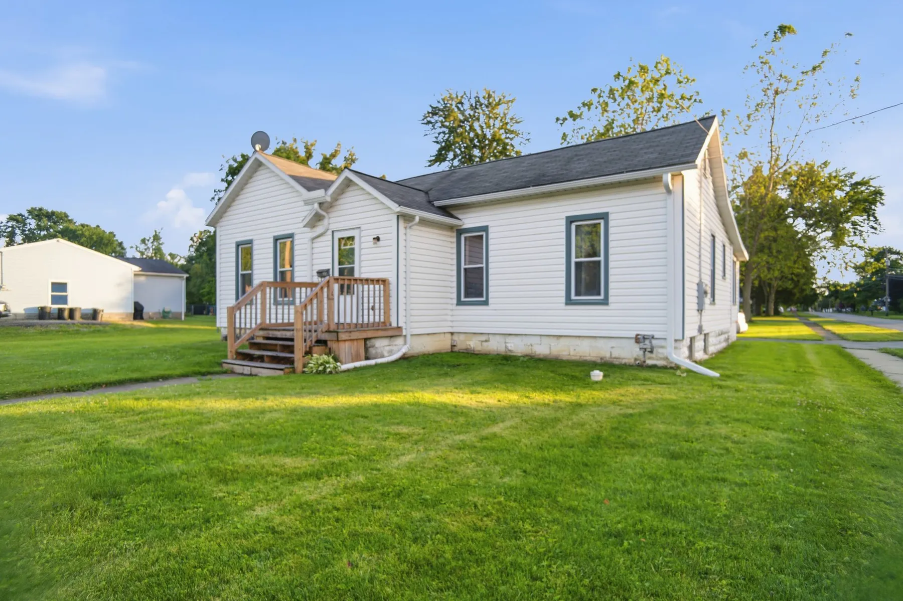 White single-storey cottage with dark green shutters and a small front deck on a green lawn.