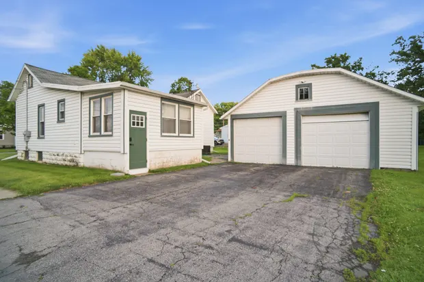 The house with its detached garage and driveway alongside a wide lawn.