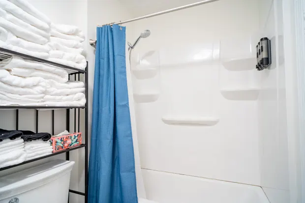 Tub-shower with a blue curtain and towel shelves.