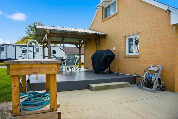Back of the cottage with a covered deck and a stone driveway with room for a boat.