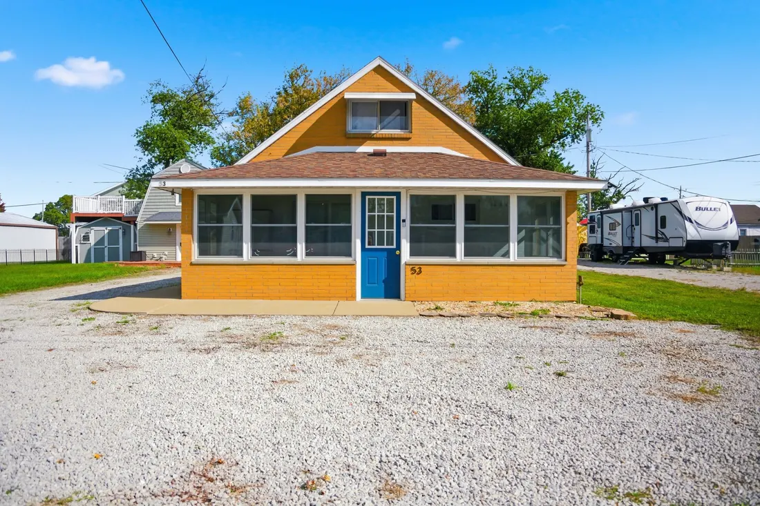 Front of the two-story cottage with an enclosed sunporch and a gravel driveway.