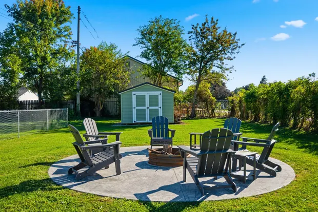 Backyard fire pit ringed by Adirondack chairs on a paved circle.