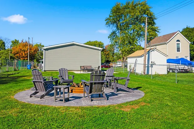 Backyard with a fire pit, Adirondack chairs, storage shed, and open lawn.