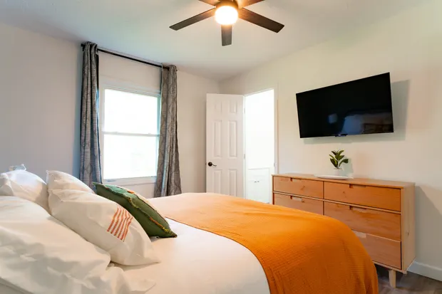King bedroom with a green accent wall, orange bedding, and windows.