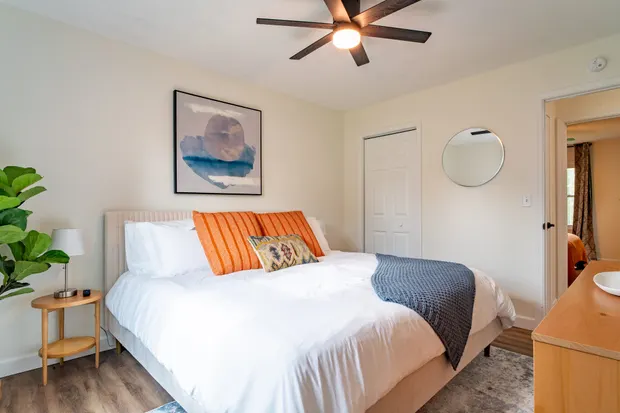 Queen bedroom with white and orange bedding and a dresser.
