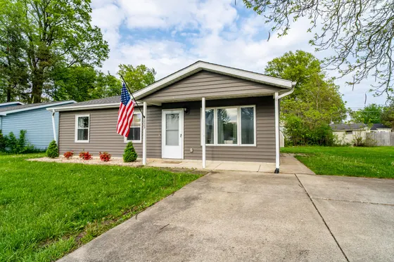 Grey single-story house with a white covered porch, American flag, and driveway.