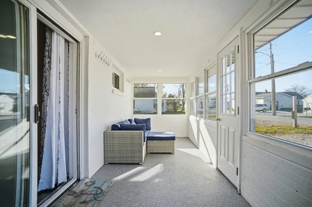 Bright enclosed porch with sliding glass doors and seating.