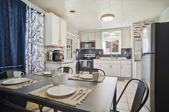 Kitchen with white cabinets, blue subway tile, refrigerator, and a dining table.