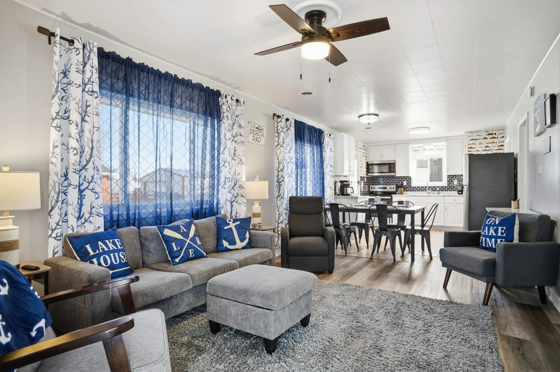 Living room with a sectional sofa, ceiling fan, "Lake House" pillows, and a dining area beyond.
