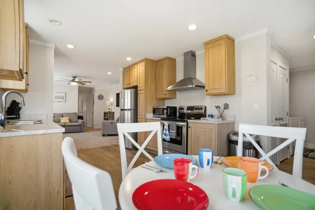 Dining table set for four with colourful mugs, beside the kitchen.