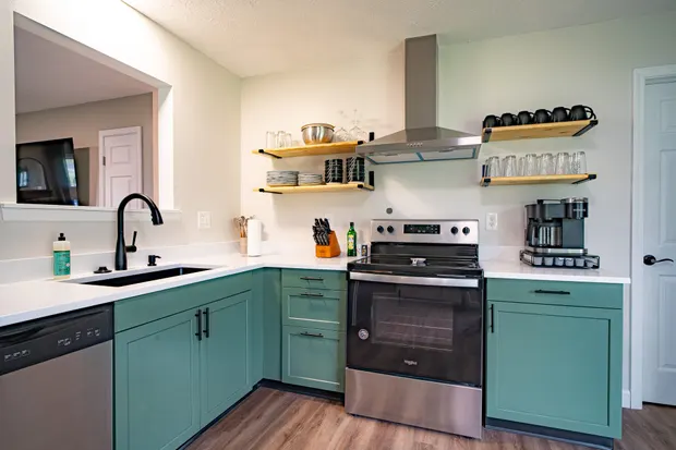 Kitchen with green cabinets, open shelves, and stainless appliances.