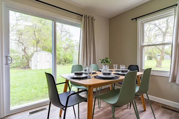 Dining table with green chairs beside glass doors to the yard.
