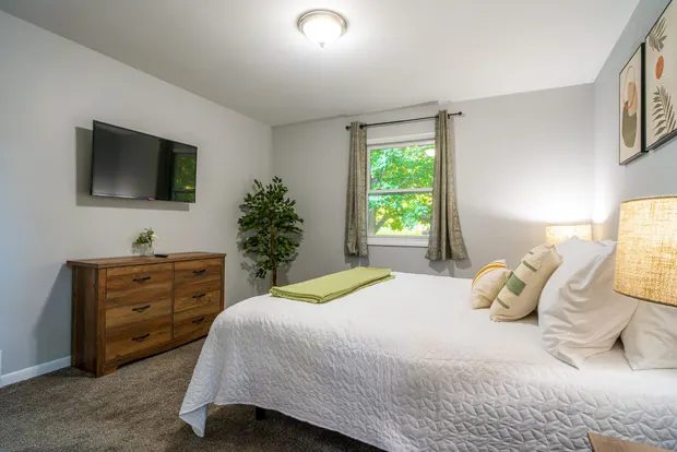 The king bedroom’s wall-mounted TV and dresser beside a curtained window.