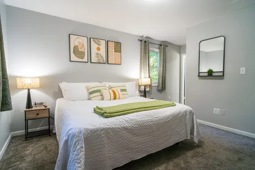 King bedroom with a wide bed, matching lamps, an arched mirror, and abstract wall art.