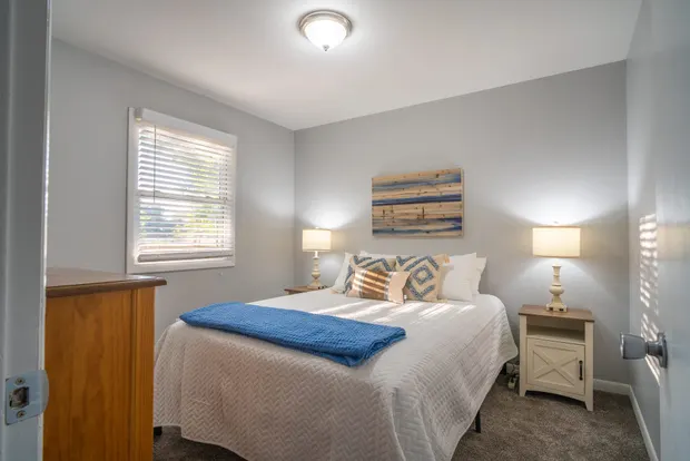 Queen bedroom with blue accents, twin lamps, and beach-themed wall art.