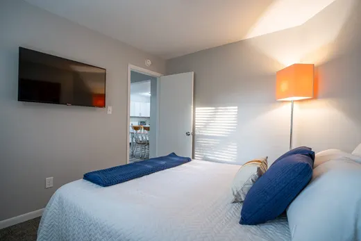 Queen bedroom with a wall-mounted TV and a door opening toward the kitchen.
