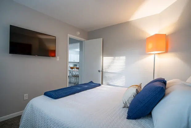 Queen bedroom with a wall-mounted TV and a door opening toward the kitchen.