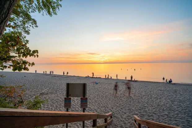 Sandy Lake Michigan beach at sunset with people along the shoreline.