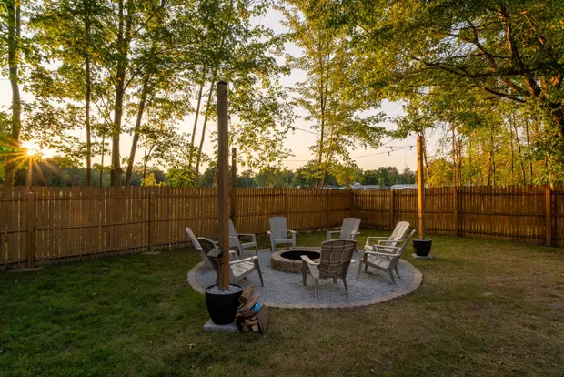 Stone fire pit ringed with Adirondack chairs in the fenced backyard at dusk.