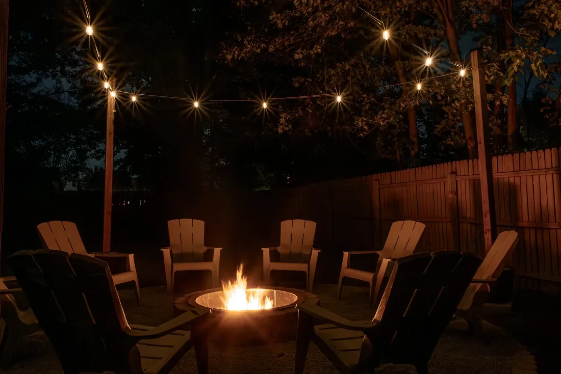 The fire pit lit at night, with a ring of chairs and string lights glowing overhead.