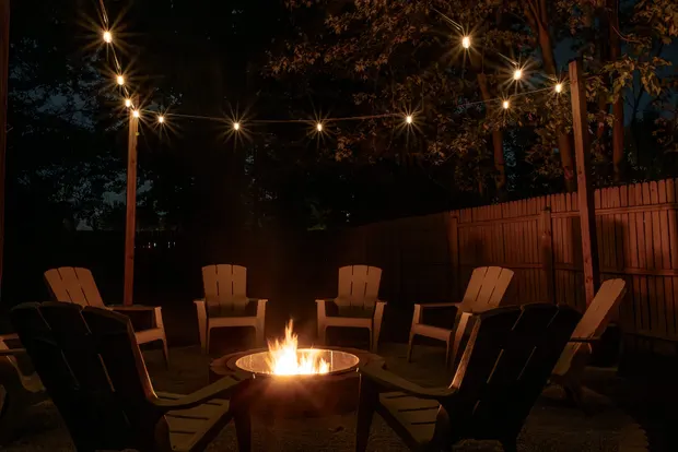 The fire pit lit at night, with a ring of chairs and string lights glowing overhead.