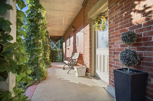 Covered front porch with brick exterior, bench, and climbing vines.