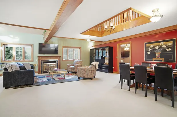 Spacious living and dining area with fireplace, wood beams, and interior balcony.