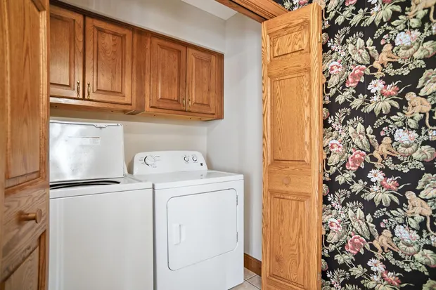 Laundry closet with white washer and dryer and upper wood cabinets.