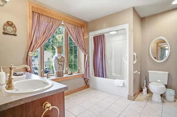 Spacious full bathroom with shower tub combo, large window, and wooden vanity.