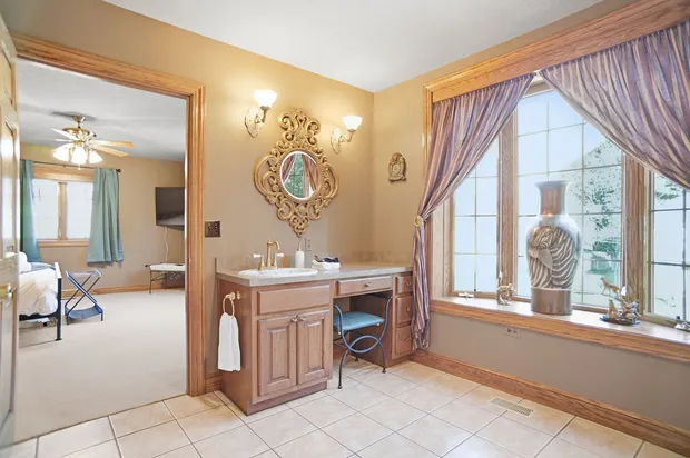 En-suite bathroom vanity with wooden makeup desk, ornate mirror, and large window.