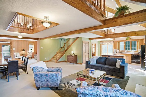 Open-concept living and dining area with exposed wood beams and open staircase