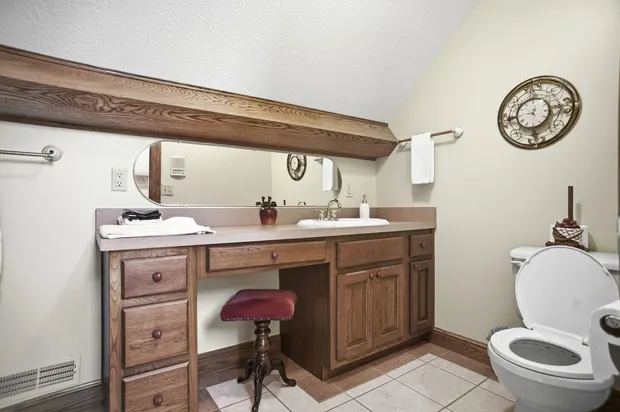 Traditional bathroom with sloped ceiling, wooden vanity, and makeup stool.