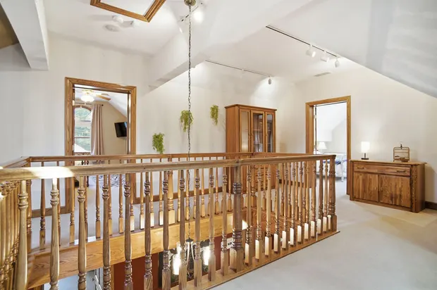 Bright upper hallway landing with wooden balcony railing and vaulted ceilings.