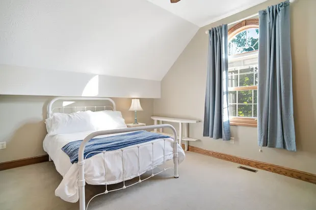 Attic bedroom with white metal bed, sloped ceiling, and arched window.