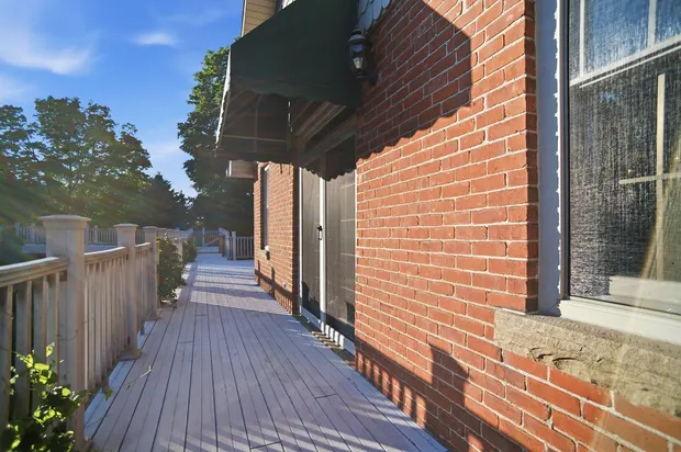 Sunlit outdoor wooden deck with red brick exterior and sliding doors.