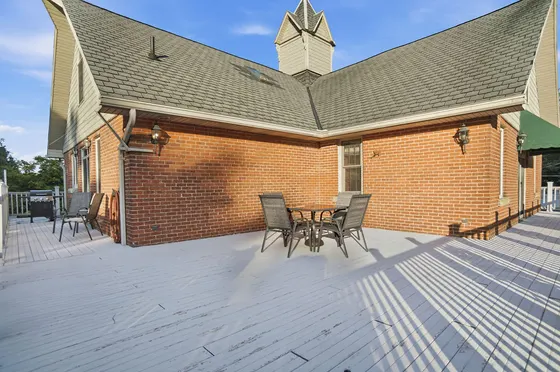 Spacious outdoor deck with dining table, grill, and brick exterior walls.