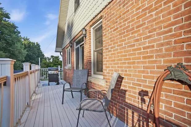 Outdoor deck with red brick exterior, patio chairs, and a gas grill.