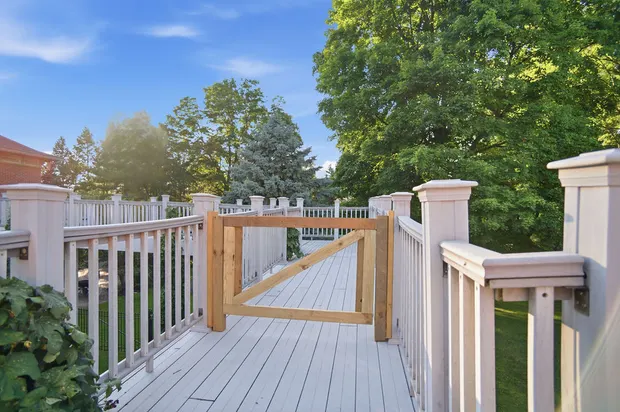 Outdoor deck walkway with white railings, wooden gate, and green tree views.