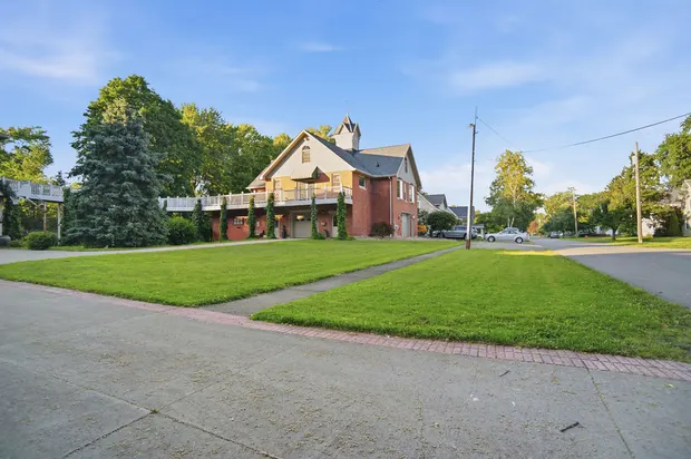 Exterior of brick home with wrap-around balcony and large green lawn.