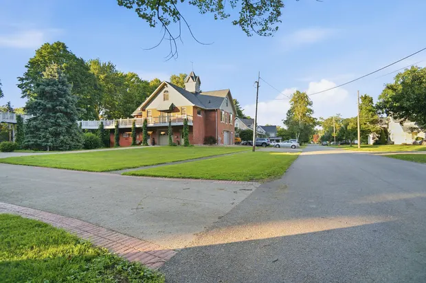 Brick house exterior with cupola, elevated deck, and large lawn on a residential street.