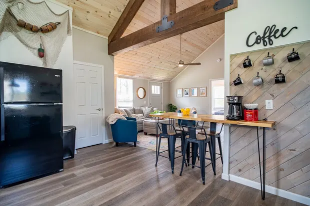 Open kitchen with grey cabinets, a coffee bar, and counter seating beside the living area.