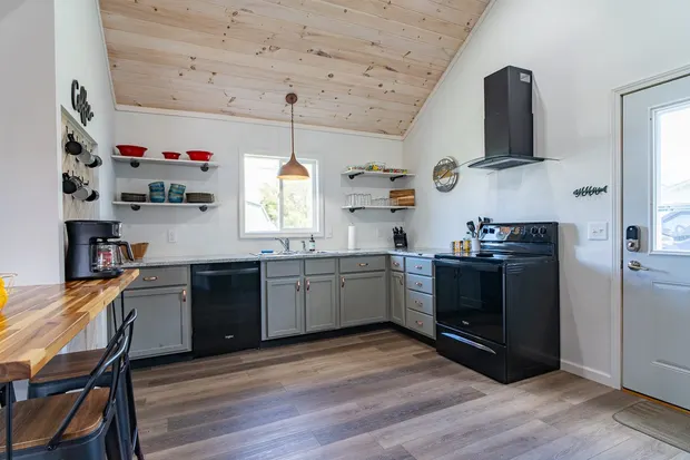 Kitchen with grey cabinets, open shelves, and a vaulted wood ceiling.