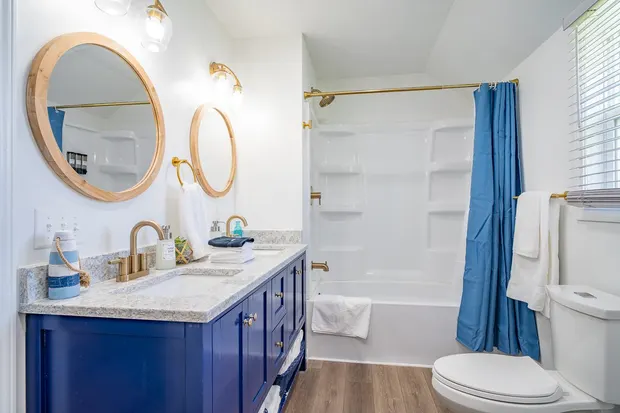 Bathroom with a blue double vanity, gold fixtures, and a tub-shower.