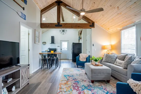 Open living room with a vaulted wood ceiling, exposed beam, and grey sofa.