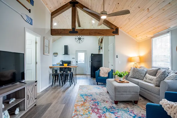 Open living room with a vaulted wood ceiling, exposed beam, and grey sofa.
