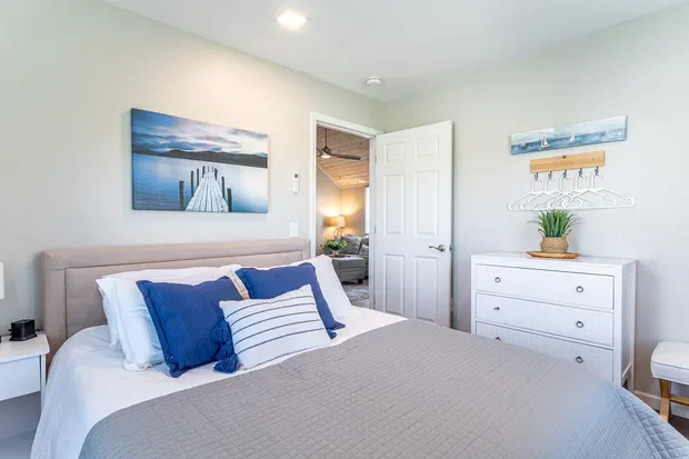 Coastal bedroom with a queen bed, white dresser, and lake artwork.